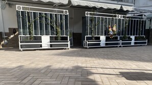 Un vaste espace extérieur doté d’un sol pavé, de deux bancs blancs et d’une clôture en métal agrémentée de plantes.