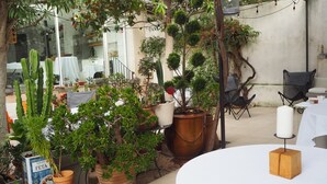 Un área de patio al aire libre con varias plantas en macetas, una mesa blanca con un candelabro y una silla negra.