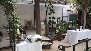 Un patio al aire libre con una mesa redonda, sillas, un brasero y diversas plantas en macetas.