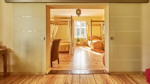 A room with a wooden floor, a bed with a canopy, a chair, and a window with curtains. - Kulturhof Dretzen (Buckautal)