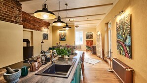 A kitchen with a central island, hanging pendant lights, a brick wall, and a large painting on the wall. - Kulturhof Dretzen (Buckautal)
