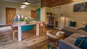 A cozy living room with a fireplace, a dining area with wooden furniture, and a kitchen with teal cabinets. - Kulturhof Dretzen (Buckautal)