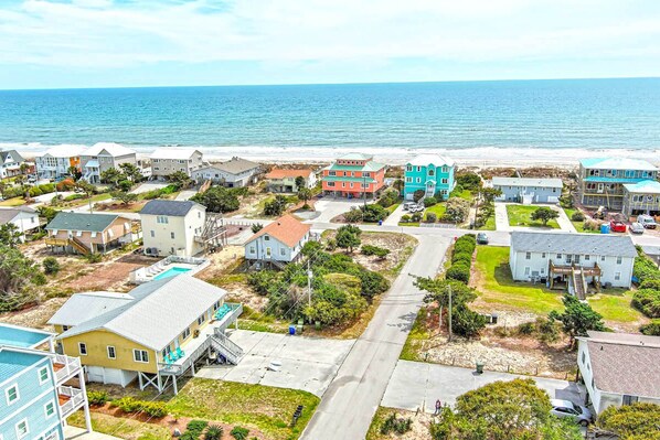 A coastal residential area with houses, a swimming pool, and a beach in the background.