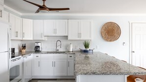 A modern kitchen with white cabinets, a granite countertop, a ceiling fan, and a woven wall decor. - Carolina House - Steps to Beach, Fantastic Location!  Walk to All Attractions (Emerald Isle)