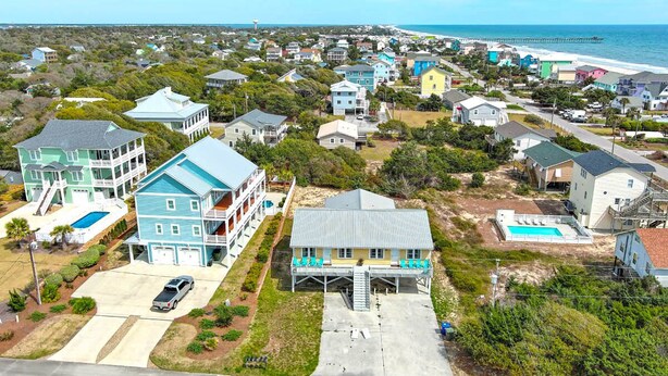 A coastal residential area with houses, a swimming pool, and a pier in the background. - Carolina House - Steps to Beach, Fantastic Location!  Walk to All Attractions (Emerald Isle)