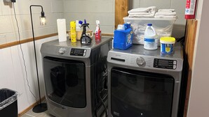 Two front-loading washing machines in a laundry room with a fire extinguisher, towels, cleaning supplies, and a power outlet. - Private apartment in a quiet neighborhood with lots of trees and privacy. (Weaverville)