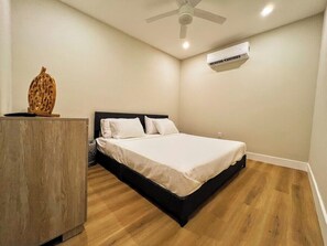 A bedroom with a bed, a wooden dresser, a ceiling fan, and an air conditioning unit.