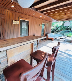 A wooden deck with a bar area, stone wall, and seating.