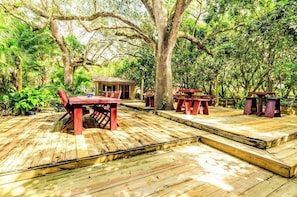 A wooden deck with picnic tables and a small building, surrounded by trees.