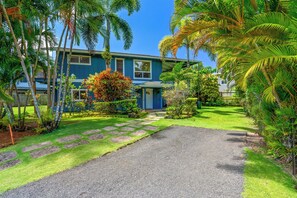 A house with a blue exterior, a gravel driveway, and a well-maintained garden with palm trees and shrubs. - Hoaloha- Few Steps to Hanalei Bay+AC & Hot Tub (Hanalei)
