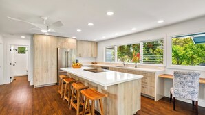 Una cocina moderna con una isla grande, taburetes de bar de madera y vistas a la vegetación por la ventana.