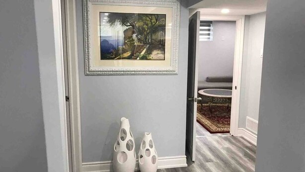 A hallway with a framed landscape painting, two white vases, and a round table with a patterned rug. - Beautiful One bedroom basement apartment (Toronto)
