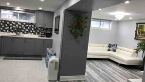 A modern kitchen with grey cabinets, a black and white backsplash, and a built-in microwave. There is a white sofa in the living area with a plant and a painting on the wall. - Beautiful One bedroom basement apartment (Toronto)