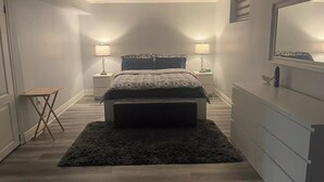 A bedroom with a bed, bedside tables, a small table, a bench, a dresser, and a mirror. - Beautiful One bedroom basement apartment (Toronto)