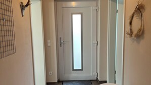 A hallway with a frosted glass door, a round white bench, a wall-mounted light fixture, and a wreath on the wall. - Modern vacation apartment with feel-good terrace in Beerfelden (Oberzent)