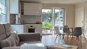 A modern living room with a sofa, a dining table with chairs, a kitchen area, and a sliding glass door leading to an outdoor patio. - Modern vacation apartment with feel-good terrace in Beerfelden (Oberzent)