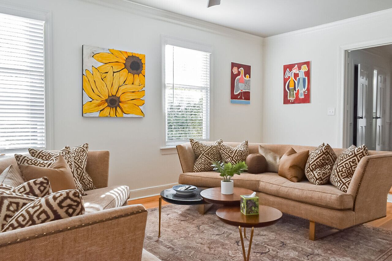 Un salon avec un canapé beige, des coussins à motifs, une table basse et des œuvres d’art accrochées aux murs.