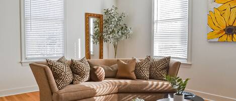 A living room with a beige sectional sofa, a round coffee table, and a large mirror on the wall.