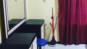 A room with a black desk, a mirror, a red curtain, and a decorative vase with sticks.