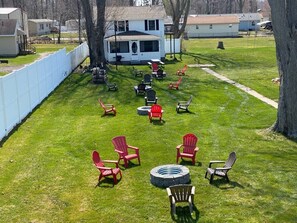 Eine grüne Rasenfläche mit mehreren Adirondack-Stühlen und einem Feuerkorb.