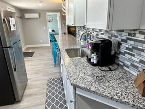 A kitchen with granite countertops, a stainless steel refrigerator, a coffee maker, and a tiled backsplash.