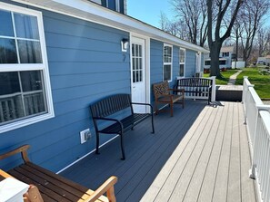 Eine Holzterrasse mit Bänken und Geländer, an einem Gebäude mit weißer Tür und Fenstern.