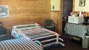 Una habitació amb dos llits, microones, una cadira i taula amb mantell de quadres.