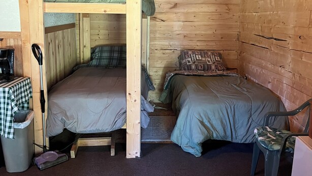 Una habitació amb lliteres, una taula amb mantell de quadres, una cadira i un gresol.