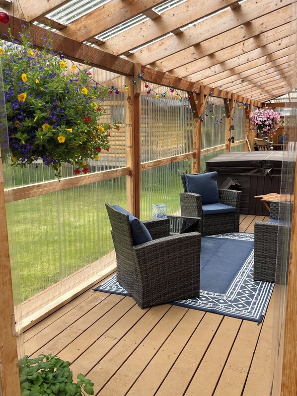 A covered patio with wicker furniture, a hot tub, and a hanging flower arrangement.