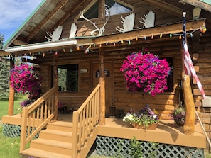 Eine Holz-Blockhütte mit Veranda, Treppe und zwei Blumenkörben.