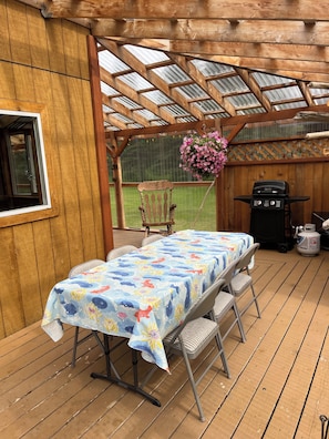 A covered patio with a table and chairs, a hanging flower basket, and a barbecue grill.