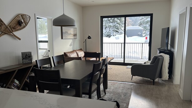 A modern living room with a dining area, a large window with a view of a snowy landscape, and a television on the right.