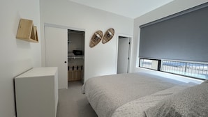 A bedroom with a bed, a dresser, a closet, a window with a view, and a door leading to another room.