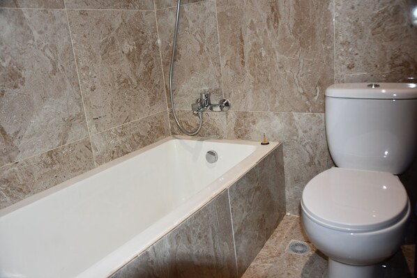 A bathroom with a bathtub, a toilet, and a showerhead.