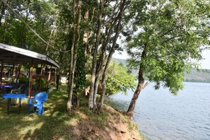 A lakeside seating area with a covered structure, tables, and chairs.