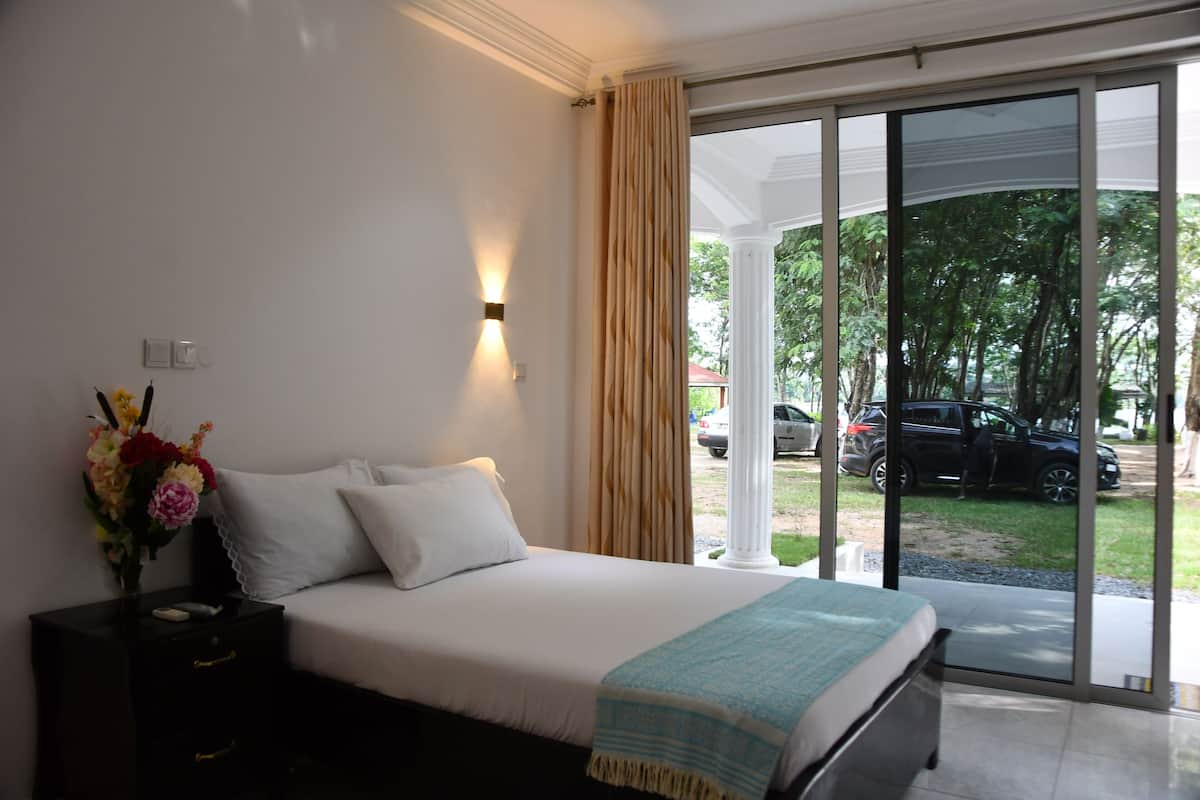 A bedroom with a bed, a nightstand with a vase of flowers, and a view of the outside through a glass door.