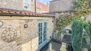 Un bâtiment en pierre avec un toit recouvert de tuiles, une porte bleue et une horloge au mur.