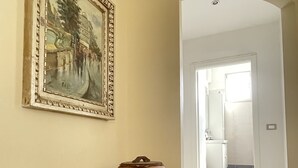 Ein Flur mit einem großen Gemälde an der Wand, einem rustikalen Keramiktopf und Blick in ein Badezimmer mit Toilette und Waschbecken.