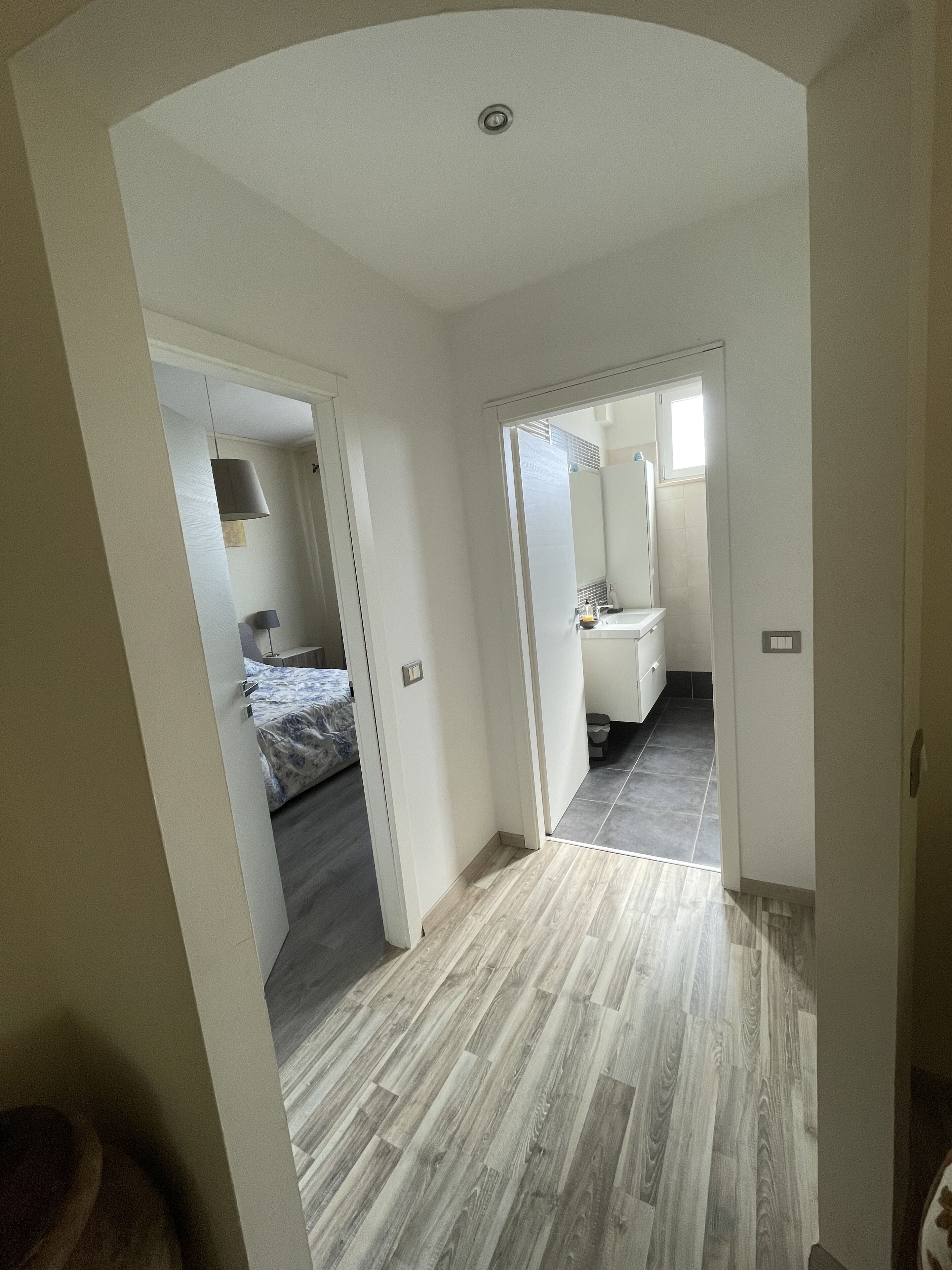 A hallway leading to a bedroom with a bed and a bathroom with a sink and mirror.