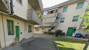 Ein Innenhof mit gepflastertem Weg, einer grünen Tür und einem Gebäude mit Balkonen.