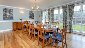 A dining room with a wooden table set for six, flanked by tall chairs, a chandelier, and large windows with curtains. - 6 bedroom accommodation in Beauly, near Inverness (Beauly, near Inverness)
