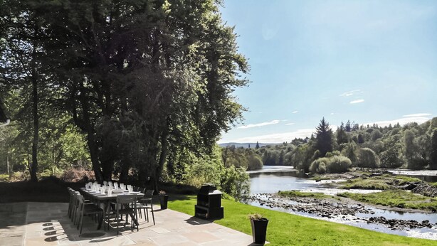 An outdoor dining area with a river view, stone patio, and lush greenery. - 6 bedroom accommodation in Beauly, near Inverness (Beauly, near Inverness)