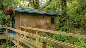 Een houten hut met een veranda en een klein raam, omgeven door weelderige begroeiing.