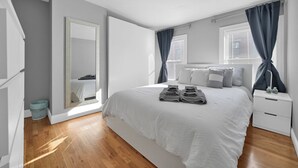 Une chambre à coucher moderne avec un grand lit, une table de chevet, un miroir et une fenêtre avec des rideaux.