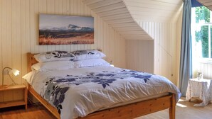 A bedroom with a wooden bed, white walls, a painting above the bed, a nightstand with a lamp, and a window with curtains. - 3 bedroom accommodation in Rockcliffe, near Dalbeattie (Rockcliffe, near Dalbeattie)