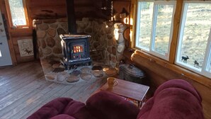 A cozy cabin interior with a stone fireplace, wooden flooring, and a window overlooking a natural landscape. - Off the grid cabin on private land surrounded by national forest. (Laramie)
