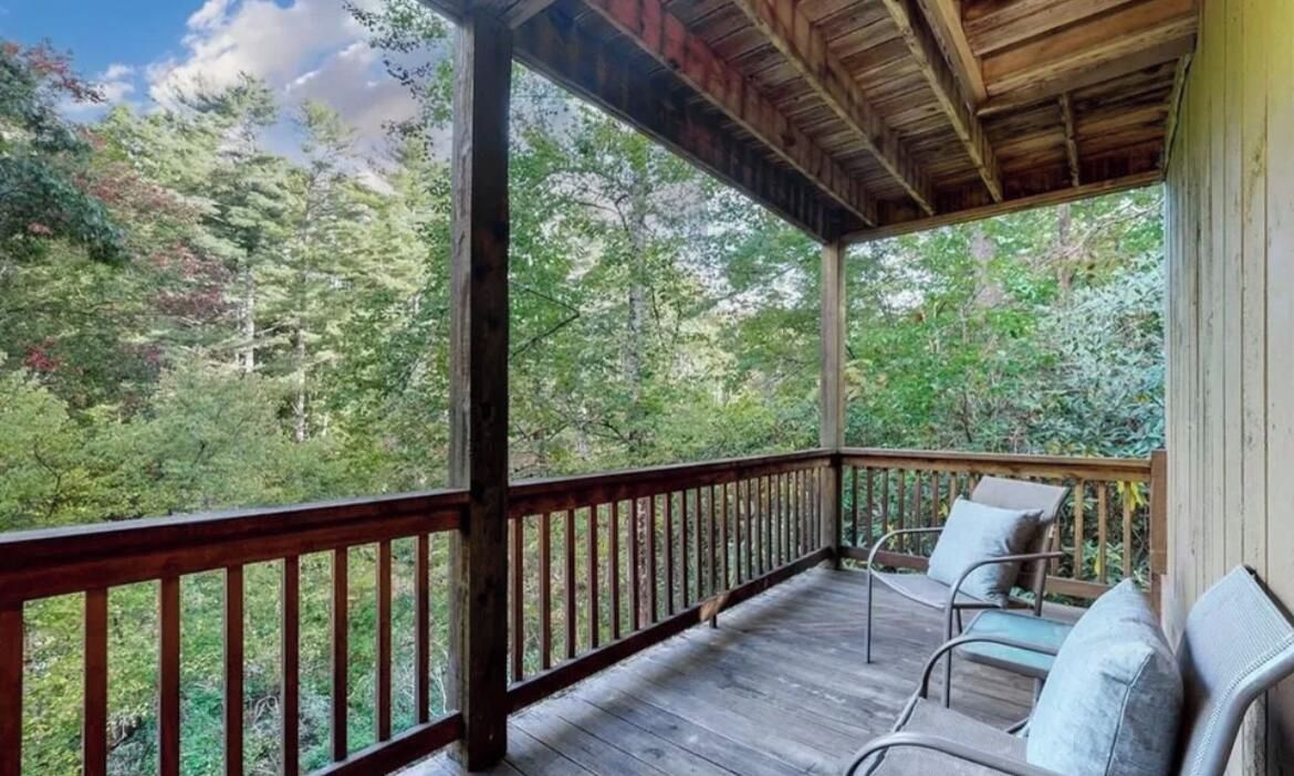 A wooden deck with a railing, two chairs, and a view of a forested area.