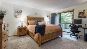 Een slaapkamer met een houten bed, een bureau met stoel, een dressoir en een raam met uitzicht op groen.