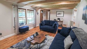Un salon avec un plafond en bois, un canapé bleu, une table basse et une vue dégagée sur l’extérieur grâce à de grandes fenêtres.