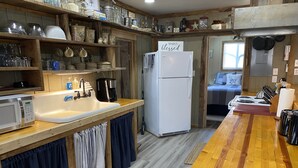 Una cocina con estantes de madera, un refrigerador blanco, un microondas y un lavamanos.